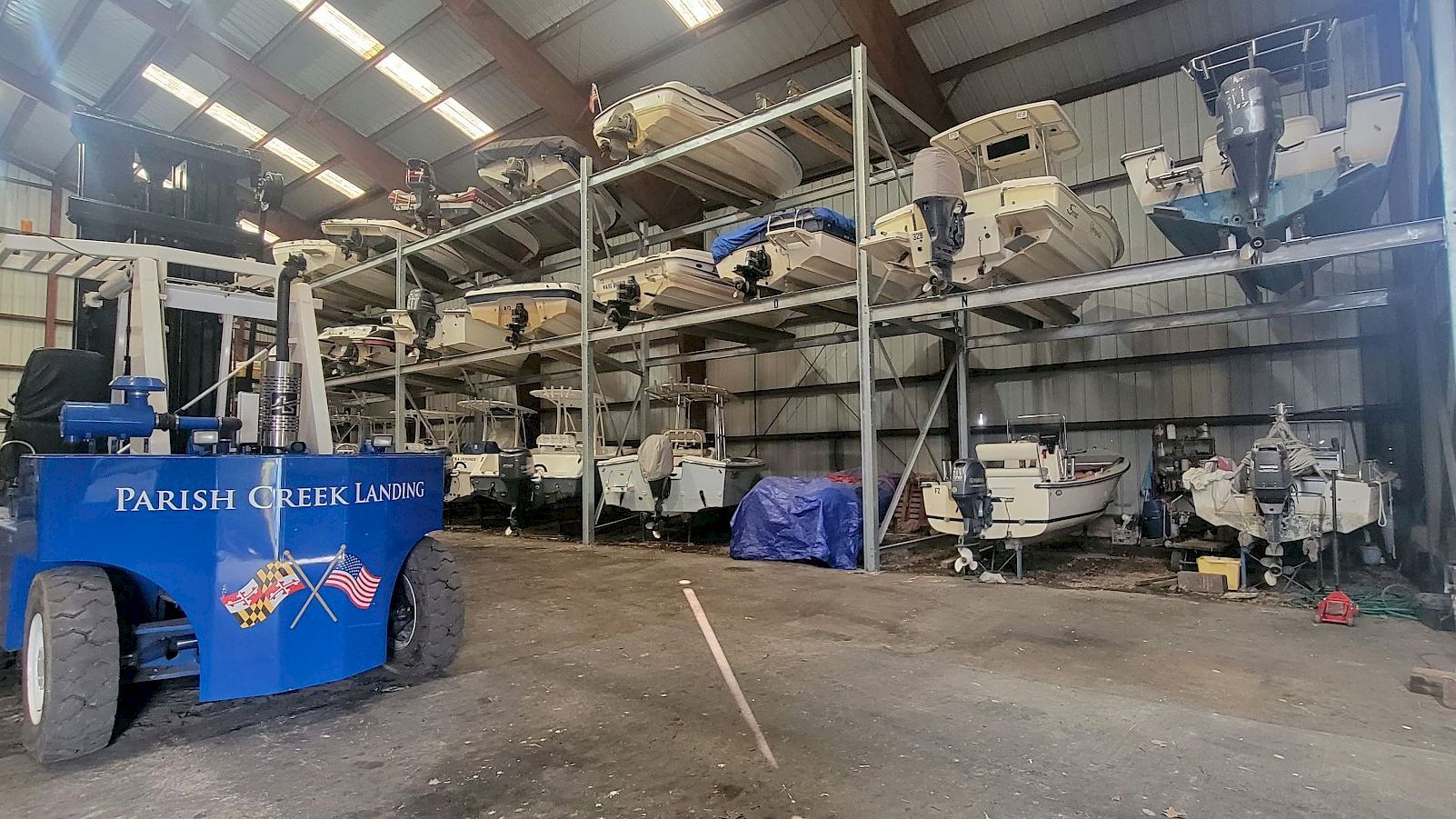 A boatyard hangar with a blue &ldquo;PARISH CREEK LANDING&rdquo; trailer and stored small boats and equipment inside a warehouse.