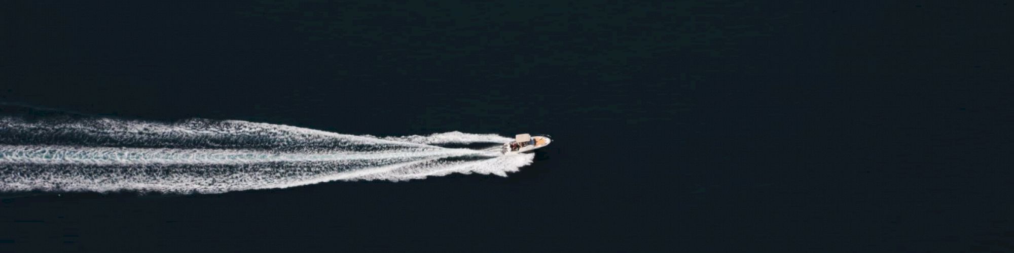 A boat cruising through dark water, leaving a trail of white wake behind it.