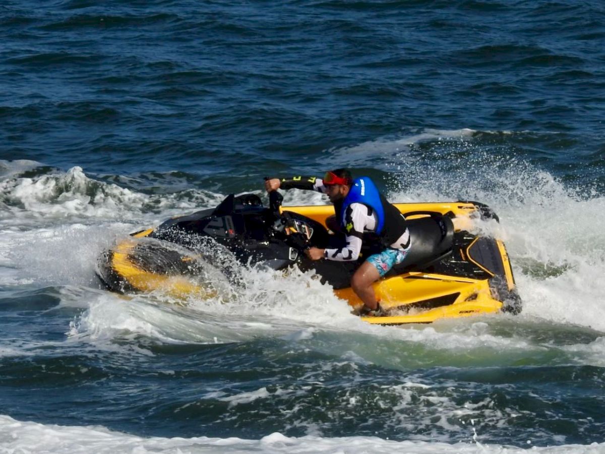 A person is riding a yellow and black jet ski on the ocean, creating splashes and waves in the water.