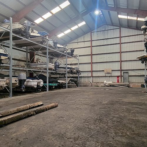 A spacious, well-lit warehouse storing multiple boats on metal racks, with several Yamaha outboard motors visible.