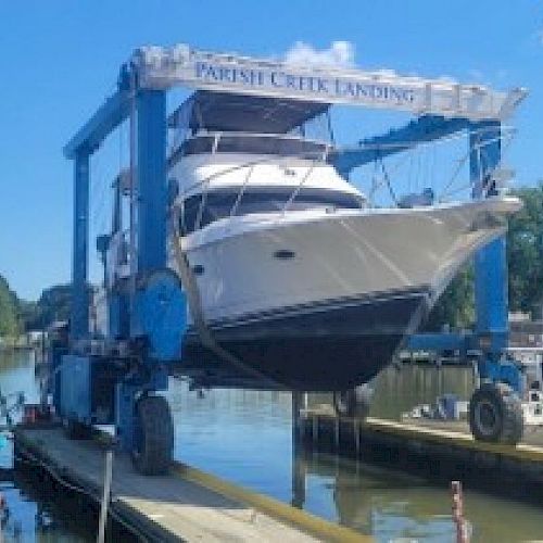 A boat is being lifted out of the water by a blue boat lift at Parish Creek Landing. The scene includes other boats and docked yachts.