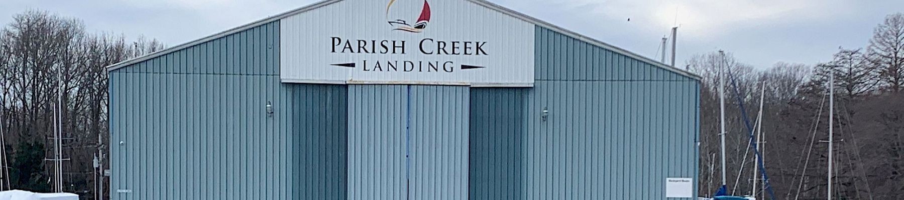 A “Parish Creek Landing” warehouse sits by a marina, with docks, boats, and calm water reflecting the building.