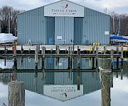A “Parish Creek Landing” warehouse sits by a marina, with docks, boats, and calm water reflecting the building.