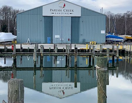 A “Parish Creek Landing” warehouse sits by a marina, with docks, boats, and calm water reflecting the building.