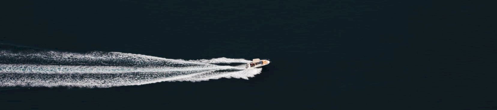 A small speedboat cuts across dark ocean, leaving a white wake behind it.