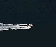 A small speedboat cuts across dark ocean, leaving a white wake behind it.