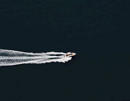 A small speedboat cuts across dark ocean, leaving a white wake behind it.