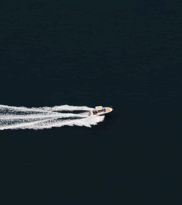 A small speedboat cuts across dark ocean, leaving a white wake behind it.