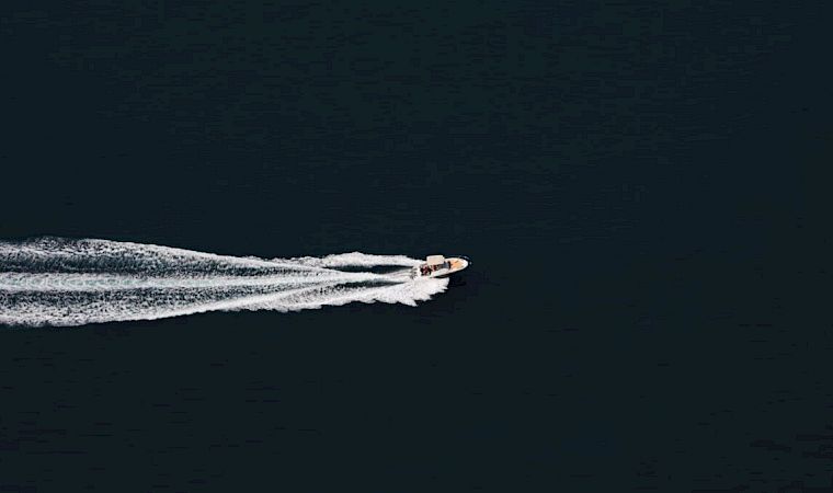 A small speedboat cuts across dark ocean, leaving a white wake behind it.