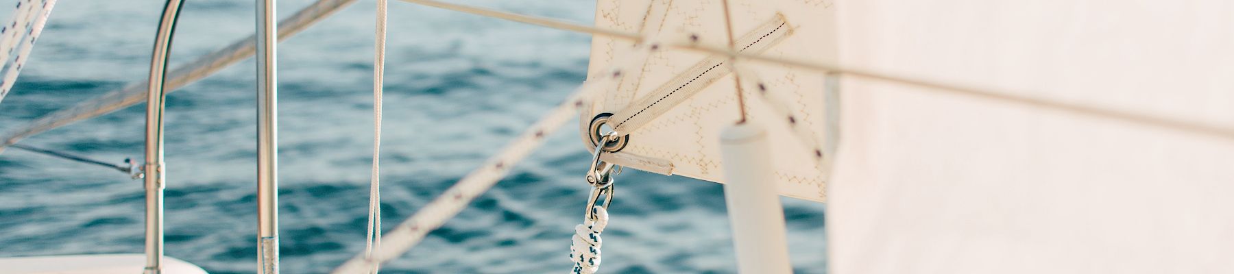 View from a sailboat with mast and rigging, a sail filled with wind, and the open ocean stretching out behind it.