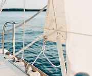 View from a sailboat with mast and rigging, a sail filled with wind, and the open ocean stretching out behind it.