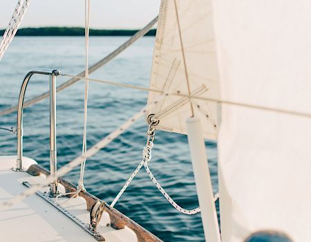 View from a sailboat with mast and rigging, a sail filled with wind, and the open ocean stretching out behind it.