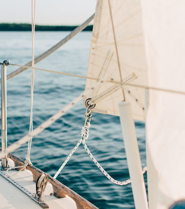 View from a sailboat with mast and rigging, a sail filled with wind, and the open ocean stretching out behind it.