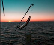 A fishing rod and lure fly above the beach at sunset, with the ocean horizon glowing behind.