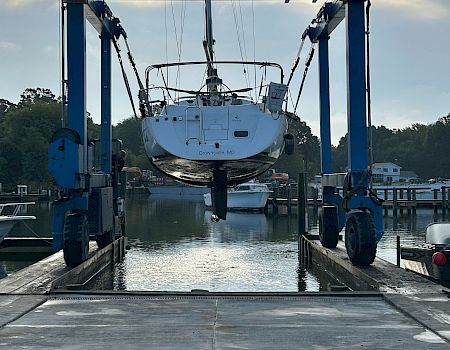 A boat named “Crownsville, MD” is lifted by a crane at Parish Creek Landing in a marina under cloudy skies.