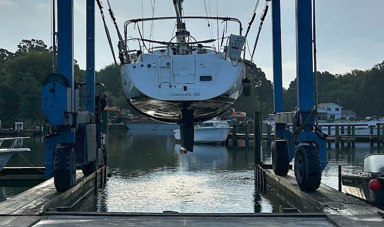A boat named “Crownsville, MD” is lifted by a crane at Parish Creek Landing in a marina under cloudy skies.