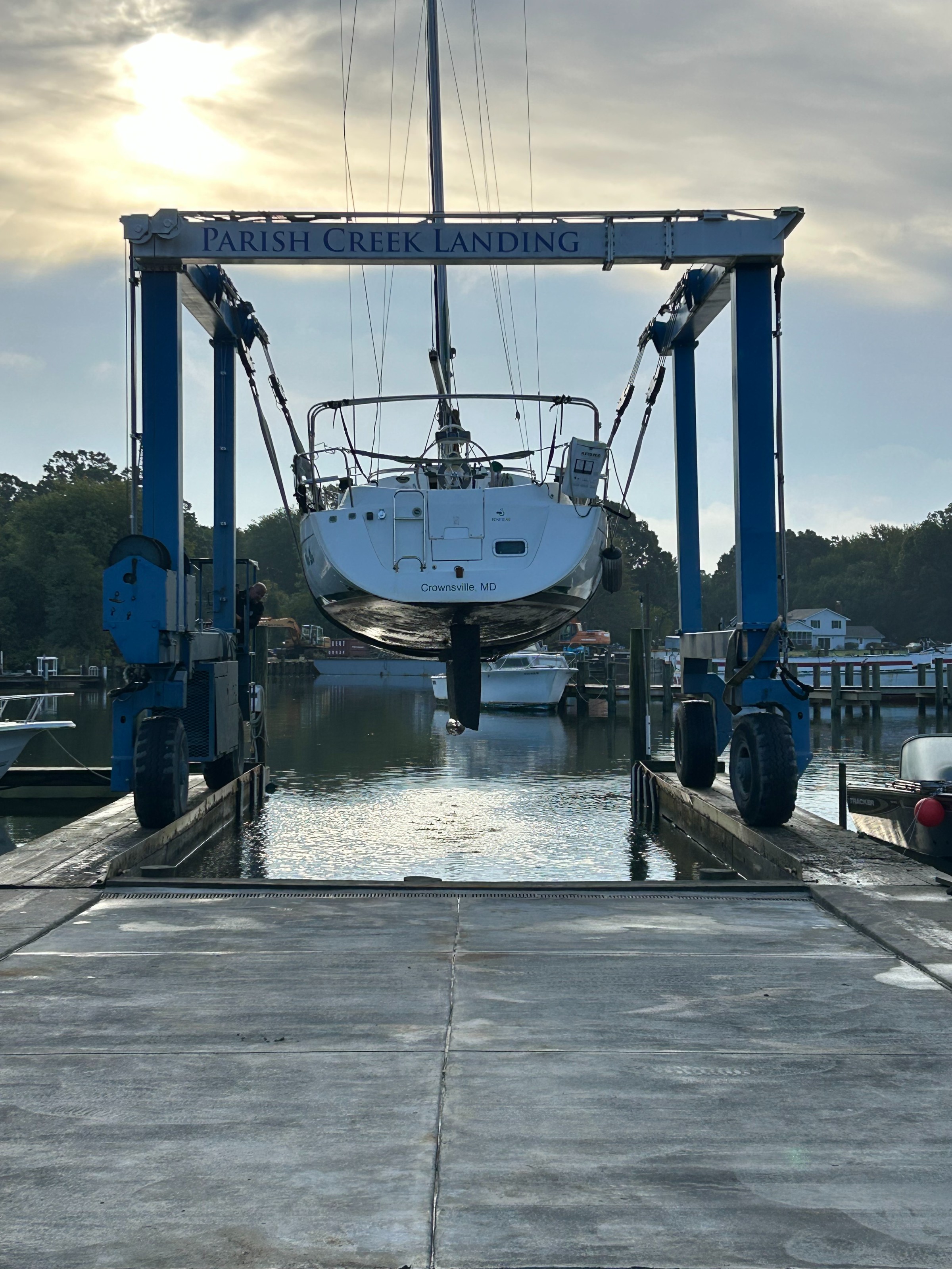 A boat named “Crownsville, MD” is lifted by a crane at Parish Creek Landing in a marina under cloudy skies.