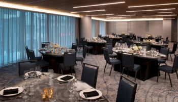 A banquet hall with round tables set for a formal event, including plates, glassware, black napkins, and floral centerpieces.