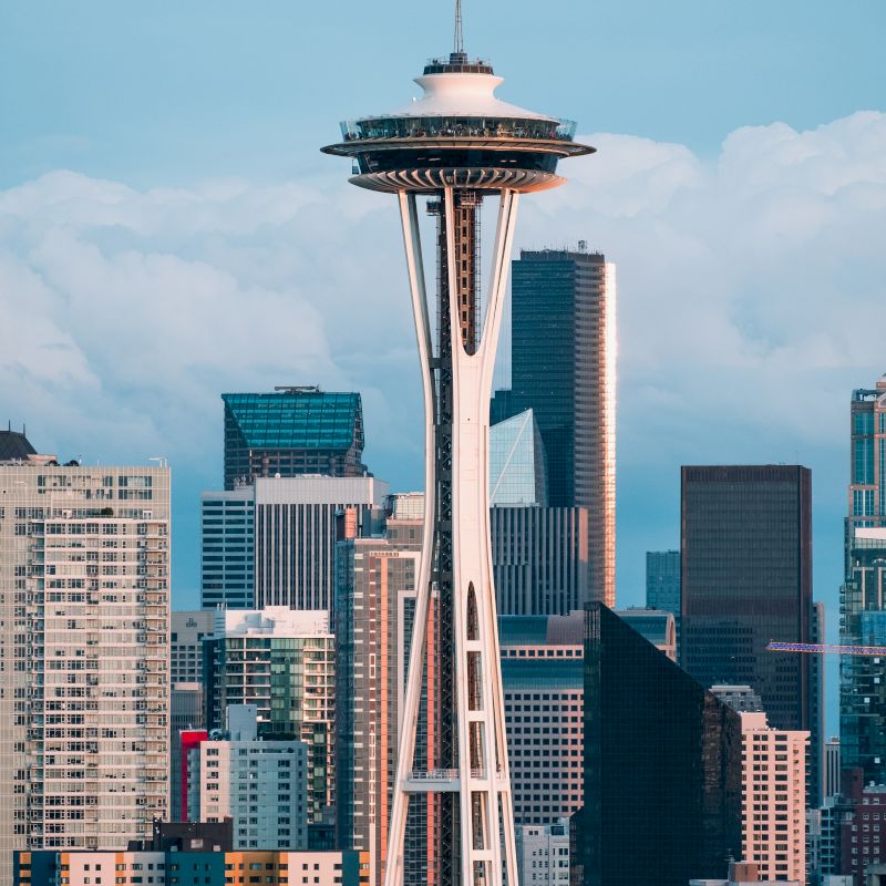 The image features the Space Needle surrounded by various high-rise buildings under a partly cloudy sky.