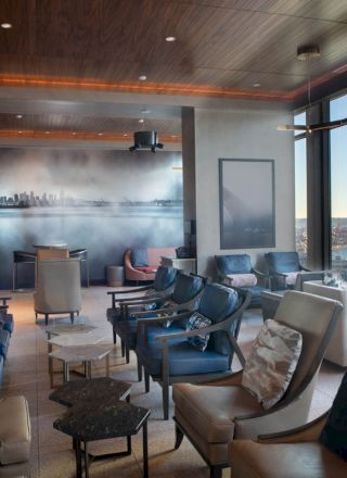 A modern lounge with a city skyline mural, large windows with a scenic view, and cozy seating arrangements.