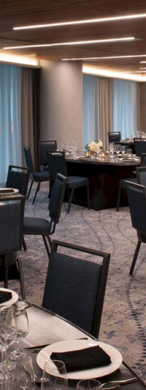 The image shows an elegantly set banquet room with round tables, dark chairs, and blue draped windows, prepared for a formal event or dining.