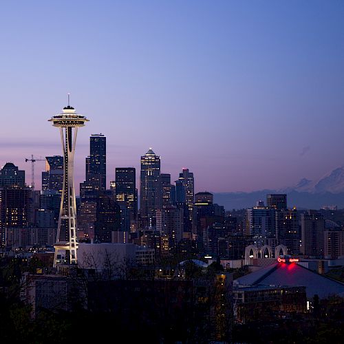 The image shows the Seattle skyline at dusk, featuring the Space Needle prominently with Mount Rainier in the background.