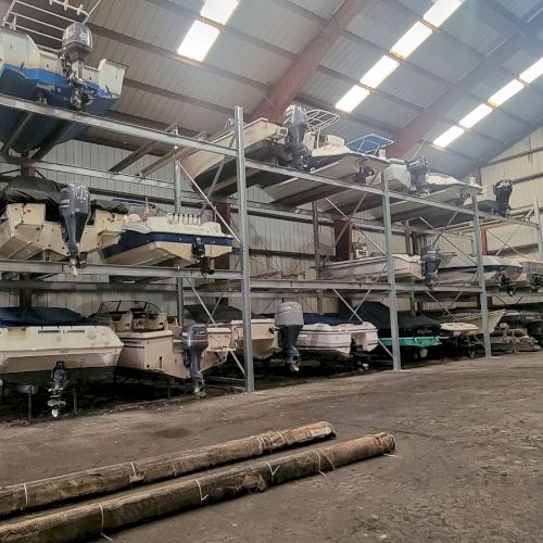 The image shows a warehouse with multiple boats stored on metal racks and some poles lying on the ground, illuminated by overhead lights ending the sentence.