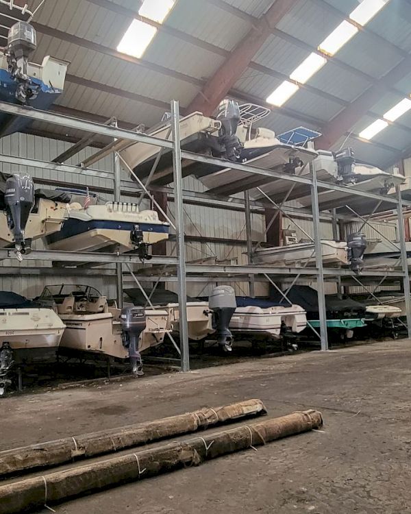 The image shows a warehouse with multiple boats stored on metal racks and some poles lying on the ground, illuminated by overhead lights ending the sentence.