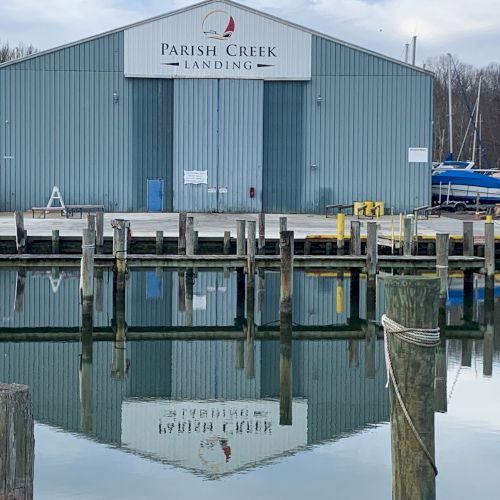The image shows a blue building labeled "Parish Creek Landing" with its reflection in the water, surrounded by docks and boats in the background.