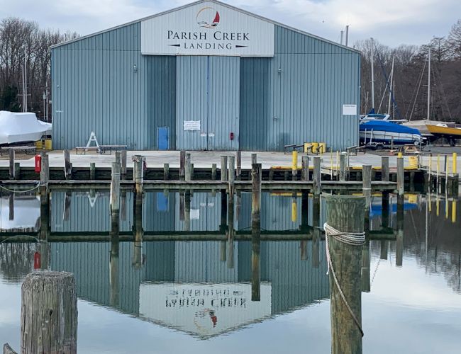 The image shows a blue building labeled "Parish Creek Landing" with its reflection in the water, surrounded by docks and boats in the background.