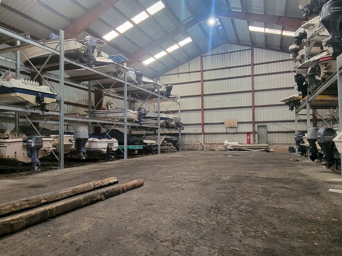 The image shows an indoor storage facility with boats stacked on metal racks, outboard motors visible; a large space in the middle ending the sentence.