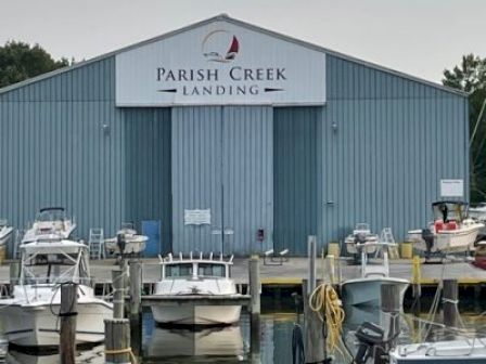 The image shows a marina with several docked boats in front of a blue building that has a sign reading "Parish Creek Landing."