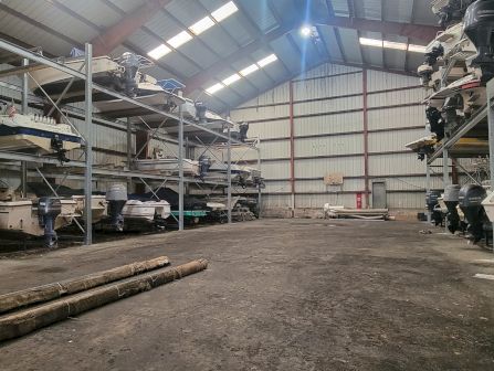 An indoor boat storage bay lined with outboard motors and speedboats on racks, with a &ldquo;keep out&rdquo; sign in the distance.