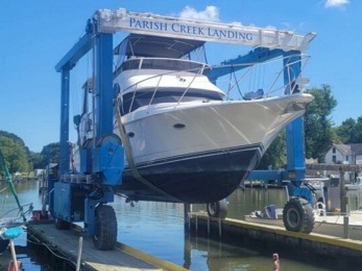 A boat is being lifted out of the water by a large mobile boat lift at Parish Creek Landing in a harbor, with nearby docks and surrounding trees visible.